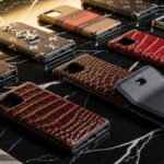 Luxury Phone cases - An overhead shot of a collection of designer phone cases on a dark marble surface. The cases feature various luxury brands and materials, including Louis Vuitton, Burberry, and embossed crocodile and leather textures.
