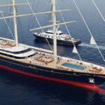 High-angle view of the massive three-masted sailing superyacht Koru with a dark blue hull and red waterline, cruising on the open ocean with a smaller shadow yacht following behind it, highlighting its size, traditional rigging, and luxury features like a deck pool.