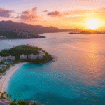 An aerial view of a resort on the coast of St. Thomas, US Virgin Islands at sunset, showcasing stunning turquoise bays, beachfront villas, and rolling green hills, with a boat sailing on the bright orange water toward the horizon.