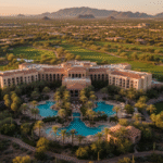 An aerial view of the Westin Kierland Resort and Spa in Scottsdale, Arizona, showing the expansive hotel building, a complex of outdoor swimming pools, and surrounding lush green golf courses, set against a desert landscape with distant mountains at sunset.