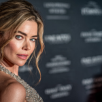 Red-carpet portrait of Denise Richards in a beaded halter gown with dangling earrings, turning over her shoulder.
