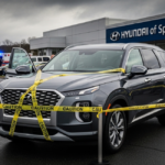 Gray Hyundai SUV cordoned off with yellow “CAUTION” tape in front of a Hyundai of Springfield dealership; emergency vehicles in background. Alt text notes this is part of the Hyundai Palisade recall response.