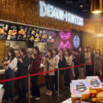 Crowded McDonald’s counter under a bright “DEMON HUNTERS” neon sign with gold tinsel backdrop—KPop Demon Hunters McDonald’s collaboration launch.