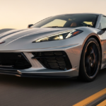 A high-resolution front-quarter view of the latest Corvette Stingray parked on a coastal highway at sunset. The aerodynamic lines and aggressive front fascia are highlighted by the warm evening light.