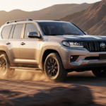 A silver 2027 Toyota Land Cruiser driving through a desert landscape, showcasing its rugged 2027 Toyota Land Cruiser features.