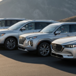 Four silver three-row SUVs parked diagonally on a paved overlook at sunrise, mountain ridges fading into soft haze behind them.