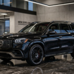 A sleek, black 2027 Mercedes-Benz SUV rests elegantly on a reflective marble floor inside a minimalist corporate showroom. The vehicle showcases a bold vertical-slat grille and intricate multi-spoke alloy wheels beneath soft architectural lighting.