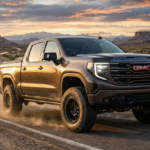 A bronze-colored 2027 GMC Sierra pickup truck drives along a winding desert road at sunset.