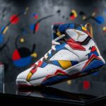Miro 7 Jordans displayed on a black pedestal with a holographic placard showing release date and price. Abstract Miró-inspired artwork in red, blue, yellow, and black forms the gallery background.